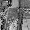 Oblique aerial photograph of Parkneuk taken from the W, centred on the cropmarks of barrows and pits, with possible quarry pits of a Roman road and the line of a military road to the left and the Dunragit cropmark complex in the top right corner of the photograph.