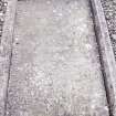 Forgan, St. Fillan's Churchyard.
General view of recumbant gravestone set in a frame. Armorial crest with two diamonds and a trefoil. A skull and bone within a roundel. Inscriptions running around the border of the stone.