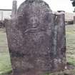 Forgan, St. Fillan's Churchyard.
General view of gravestone. Stone with curved top, head of a man in a periwig, with a shuttle below and two discs.