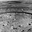 Excavation photograph. Stone circle XI from the S. Stones numbered clockwise 1 to 10 beginning with the tallest at the left side. Stone 5 has fallen and is lying out of position. F210 the central burial pit is excavated immediately N of the ranging poles.