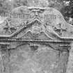 View of West face of gravestone commemorating Patrick Proudfoot and Janet Hunter d.1742, in the churchyard of Glencorse Old Parish Church, showing 'Green Man' face and 'MEMENTO MORI' legend above a tympanum filled by a winged cherub.