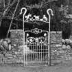 Detail of wrought iron gateway to garden on E side of road with crook and lambs overthrow, 'C H' monogram and naturalistic plant forms.