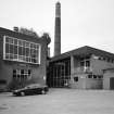 Alloa, Whins Road, Brewery
View from SE of brewhouse (with grist case no. 2 on roof, right), chimney and boiler house block. The bore hole housing is the flat roofed building on the right. The bore hole provides water for cooling the refrigeration compressors. The water for brewing is taken from the mains and is filtered through the Candy water filtration system on site