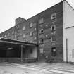 Alloa, Whins Road, Brewery
View from NNW of brick and concrete four-storey and basement, ten by four bay Barns Block grain handling area. Note railway lines in foreground. Grain originally came in by rail by means of a branch line from the Edinburgh-Stirling Line which ran along the N side of the brewery site. Latterly, grain was brought in by road. The grain is unloaded into the hopper opening visible between the rails (foreground) and is moved by an elevator system up to the top floor of the grain handling area. This building still carries the (painted out) name of the Arrol family who were involved in operating the brewery from 1866 until 1951