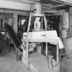 Alloa, Whins Road, Brewery, Mill Room area, top floor, interior
View showing intake and distribution area of mill room area. Note intake duct carrying malted barley mix from the fourth floor of the Barns Block c.120 metres away. The grain is conveyed to the Buhler destoner, in the foreground of the picture, which sorts out foreign bodies from the malt mix by vibrating at a rate of 4000 r.p.m. Any foreign bodies (metalwork, stones etc.) falls into a sack attached to the mouth of the destoner of which can be seen in the foreground. The malt to be milled is removed by means of a 'screw' visible in the middle foreground and conveyed to a screen below which feeds the Miag malt mill