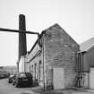 View from SE of SE end of boilerhouse, also showing the associated chimney stack in the background.  Part of the boilerhouse wall, centre, beneath chimney, has had to be replaced with a crimped steel shell.