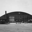 View from NE of NNE end of hangar, showing brick gable with windows and door and brick chimney stack		