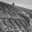 Detailed view from SE of centre part of hangar, showing exposed fabricated steel shell (left), with adjacent relatively intact outer layer of concrete, covered with bitumen