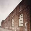 View from North East of South East frontage of works (onto Den Road), showing pilasters and segmentally-arched windows with moulded brick arches.  Note that the works was formerly a foundry, but later became a felt mill for Nairn's of Kirkcaldy