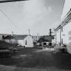 Bowmore Distillery
General view from SE within W yard of the distillery, showing SW end of floor maltings (right), still house (centre), and offices (left), with bonded warehouse block in the background