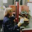 Building D15 (NS 2940 3994): Detail of Brenda Cain operating one of two dipping frames, on which racks of fusehead combs are dipped in sequences of dip mixtures to make up the required fusehead compound. The different dips are colour-coded, and the fusehead (which now resembles a match head)  is protected by outer layers to prevent accidental combustion. Note that the dips are prepared in aluminium pans in building D13, which in part resembles a kitchen, and which requires the use of solvents
Photosurvey 27 August 1995
