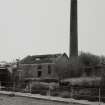 View from NW of chimney and possible former boilerhouse to S of works, on opposite (S) side of River Garnock, photographed 23 April 1992