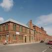 General view from SW of SW corner of works, showing elevations onto Norman Street (left) and French Street (right).  The view also shows the coloured enamel bricks decorating the office building occupying the SW corner of the works