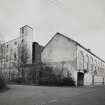 View from NW of frontage of former stationery warehouse, fronting onto Forneuk Street, with former cotton mill partially visible (left).  An addition to the N end of the mill (built in 1914) is also visible