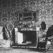 Interior. Drawing room decorated with damask wallpaper, showing a view of a small fireplace flanked by two large chairs.