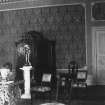 Interior. Detail of a room showing various pieces of furniture, against a backdrop of damask wallpaper, encased by a panel.