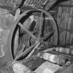 Interior.
Detail within sawmill showing part of feed for sawbench in foreground, and large flat-belt pulley behind.