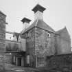 View from NE of two Kilns, W end of Maltings, and overhead walkway between the two buildings.  Note also the wind vanes on the two kiln ventilators