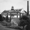 Exterior view from SW of former cooperage, also showing boilerhouse chimney, and examples of topiary typical of the distillery gardens