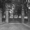 View from S showing set of four Edwardian classical stone gatepiers topped with urns with gates and flanking railings.