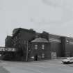 General view from NW of W end of S block of factory, showing (L to R) West Gangway over Drumfrochar Road (building no. 27, NS2783 7544), Granulating/Drying/Cooling (building no. 9, NS2787 7542), Sieving & Bag Filling (building no. 8, NS2784 7543), gatehouse (building no. 4, NS 2782 7544) and East Warehouse buildings (building no. 25, NS 2784 7540)