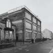 General view from E of main facade of factory, also showing part of the SE side of the factory which is also rubble faced and bears a 1921 dateplaque
