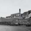 General view of the factory from W, showing its short boilerhouse chimney, and more modern steel-clad additions to the factory