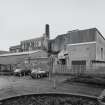 General view of the factory from W, showing its short boilerhouse chimney, more recent steel-clad additions to the factory, and a new block occupying its SW end