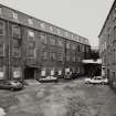 View from N across wedge-shaped yard dividing two four-storeyed polychrome-brick mills at centre of works.  Photosurvey 22-APR-1992