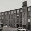 View from NE across wedge-shaped yard towards E elevation of polychrome-brick four-storeyed mill ( W mill).  Photosurvey 22-APR-1992