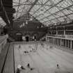 Interior view from ENE of swimming bath, showing traditional pool-side cubicles, upper gallery for spectators, and curved mild-steel trusses supporting glazed roof