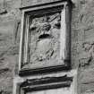 Armorial panel over doorway in exterior gable-end of S burial-aisle.