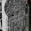 Medieval coped grave-cover bearing floriate-headed cross, currently standing within S wall of church at W end.