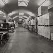 Cased Goods Store: View from NW of cased whisky awaiting dispatch (right), and filmwrap department.  Pallets of whisky boxes are conveyed by hoist and overhead gantry conveyor to neighbouring cased goods store.
Photographed 27 January 1994