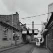 View from S between Wire Division's North Mill (left) and W end of Broadloom Department (right), with boiler house chimney in the background